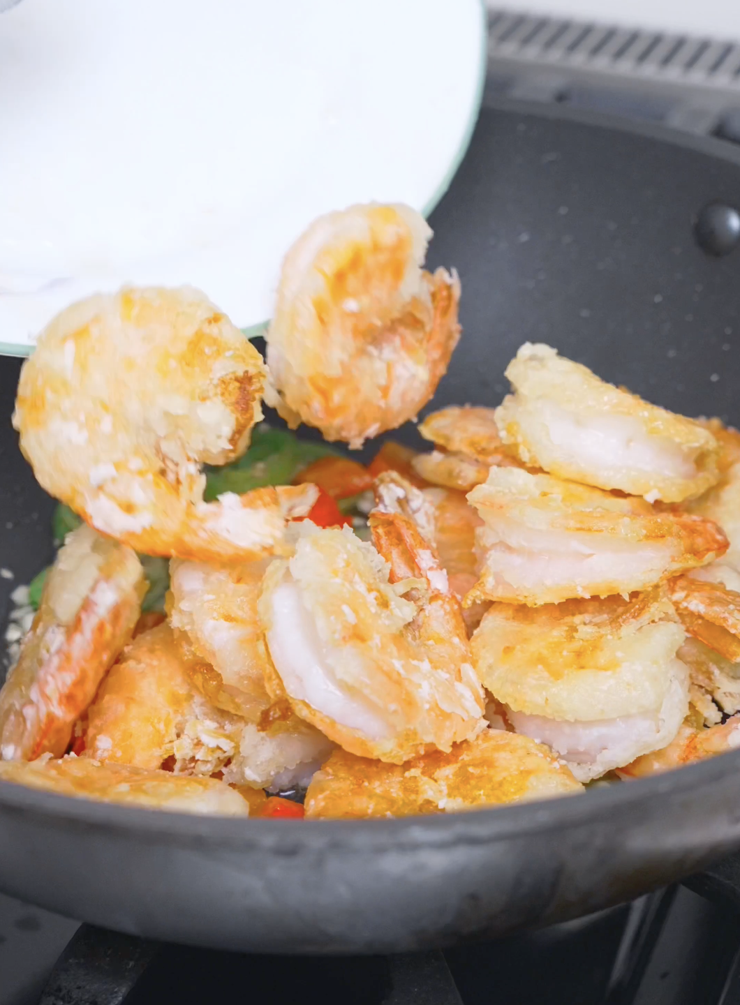 Crispy fried shrimp being tipped back into the pan with the peppers for Salt and Pepper Shrimp Recipe.
