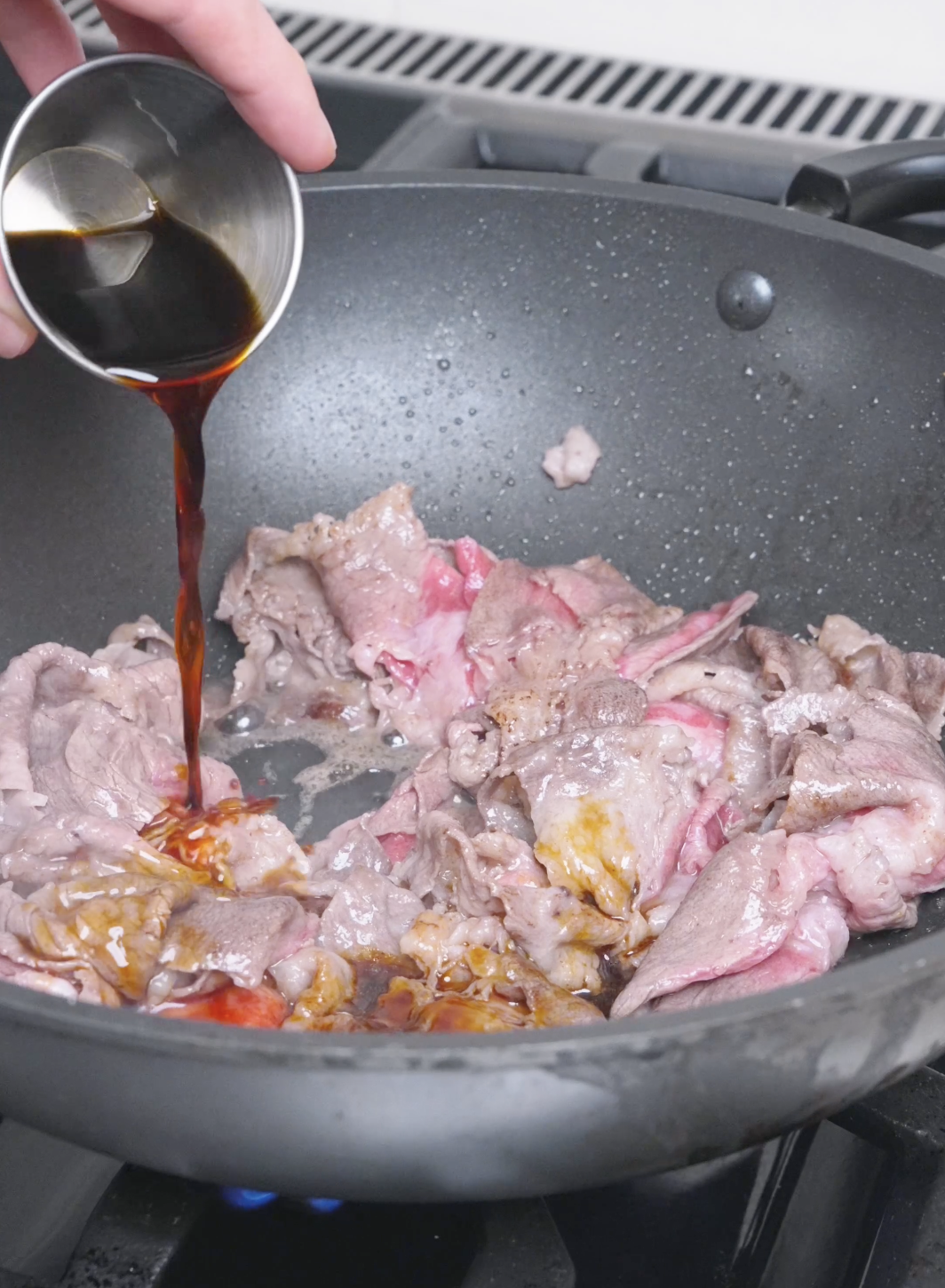 Soy sauce being poured over the browning beef in the pan for Beef Udon Recipe.