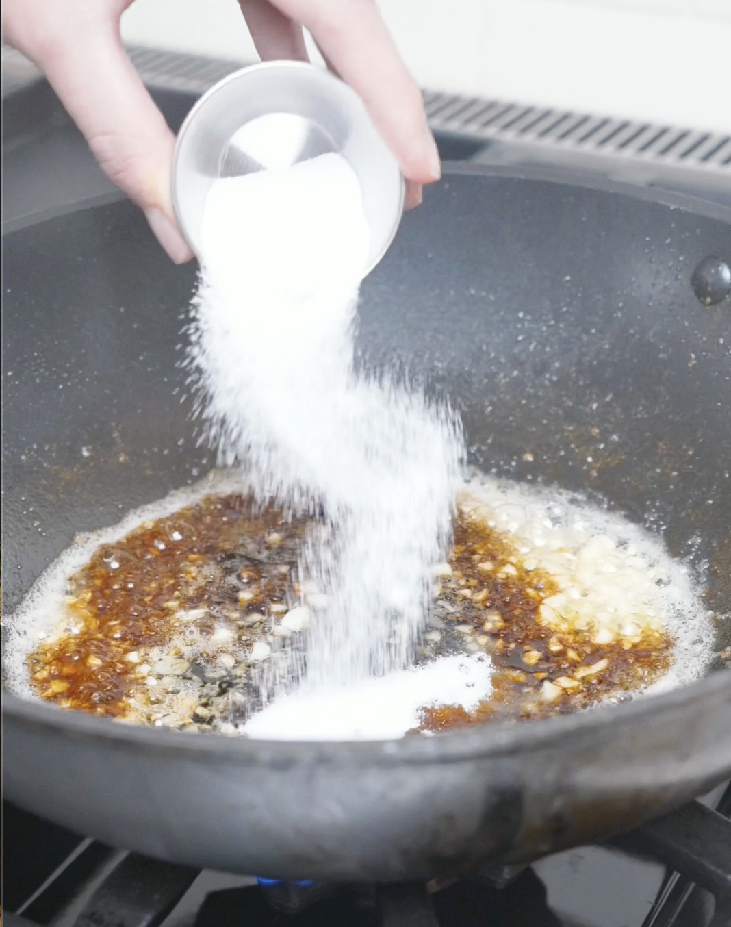 Sugar being poured into the garlic, butter, and soy sauce in the pan for Garlic Butter Shrimp Recipe.