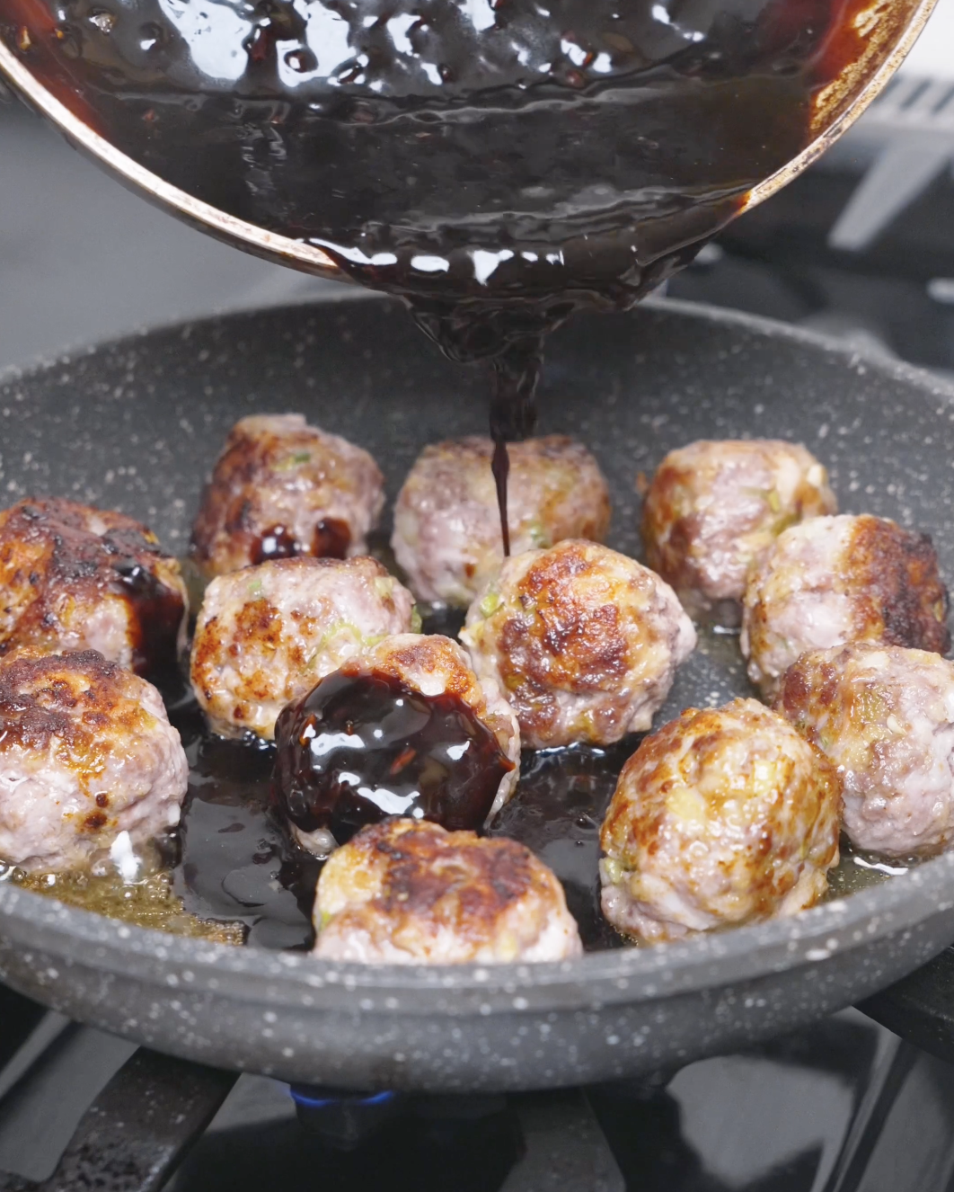 Thickened teriyaki sauce being poured over the browned meatballs in the pan for Teriyaki Meatballs Recipe.