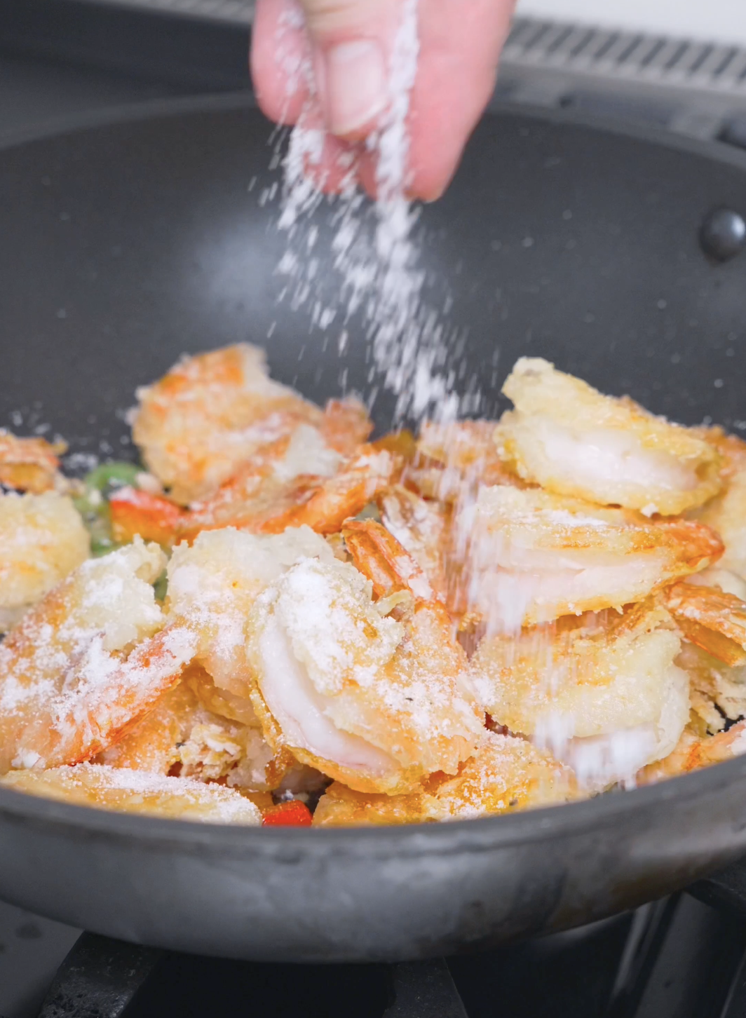 The salt, sugar, and pepper mixture being showered over the shrimp for Salt and Pepper Shrimp Recipe.