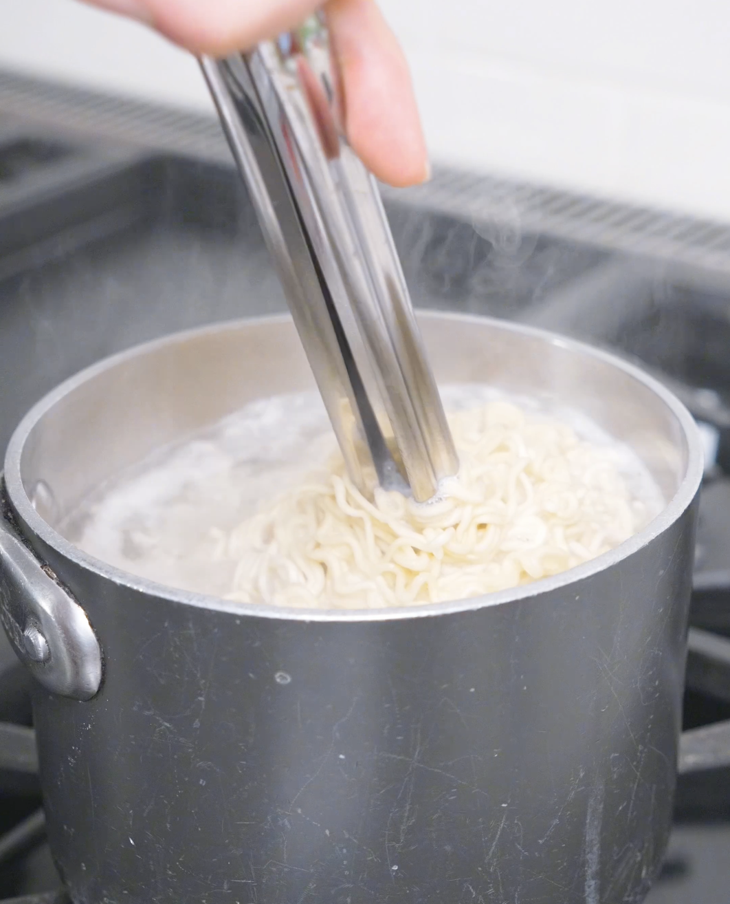 Ramen noodles being loosened with tongs in a pot of boiling water for Creamy Curry Noodles Recipe.