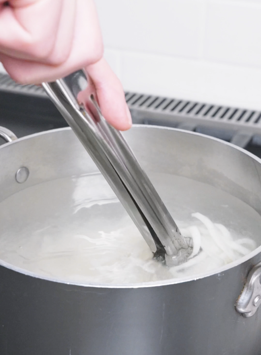 Udon noodles being separated with tongs in a pot of boiling water for Beef Udon Recipe.