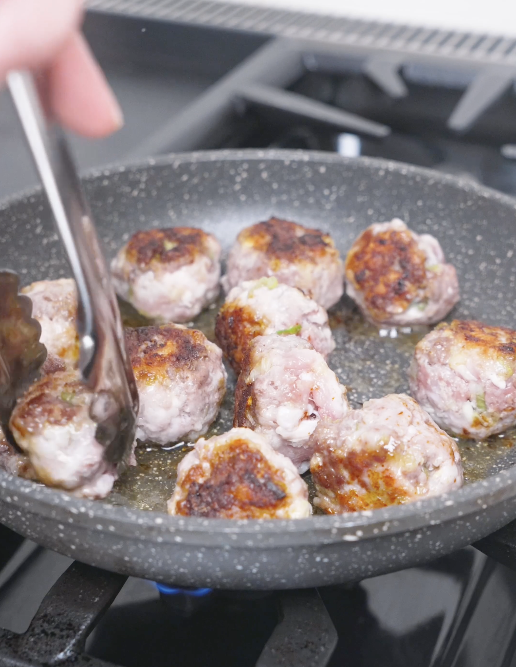 Meatballs being rotated with tongs so they brown evenly on all sides for Teriyaki Meatballs Recipe.