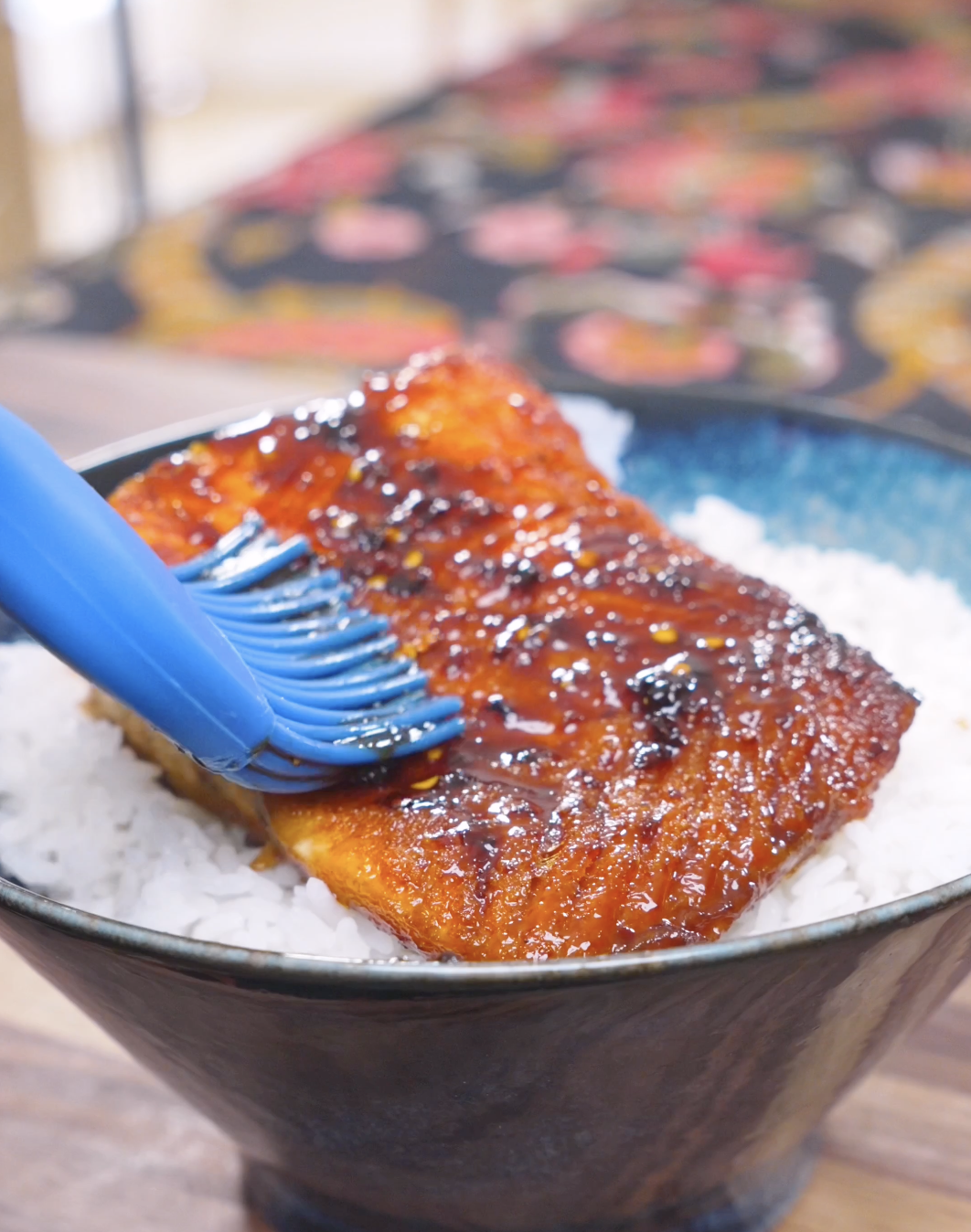 A basting brush spreading extra chili crunch glaze over the salmon on rice for Spicy Salmon Bowl Recipe.
