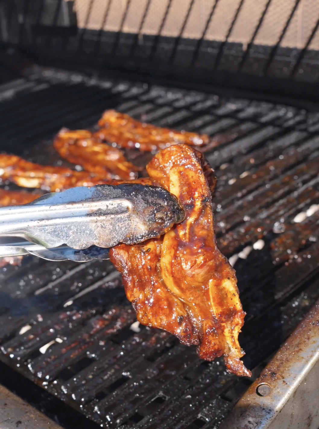 Tongs lifting a short rib with caramelized, charred edges off the grill for Korean BBQ Short Rib Recipe.
