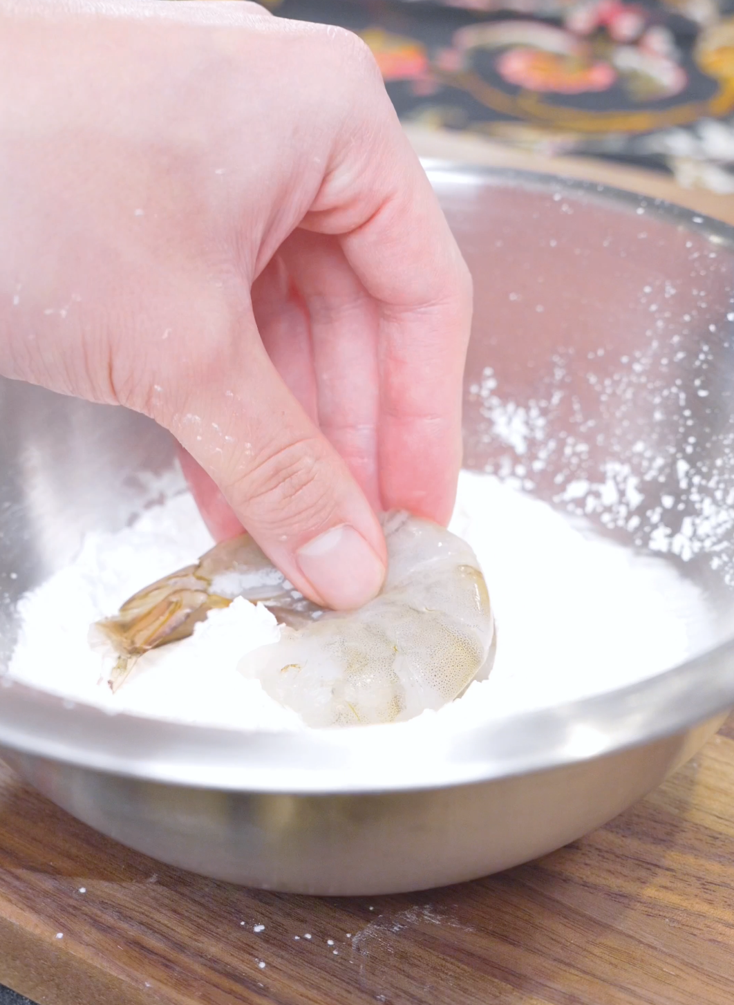 A shell-on shrimp being pressed into a bowl of cornstarch for Salt and Pepper Shrimp Recipe.