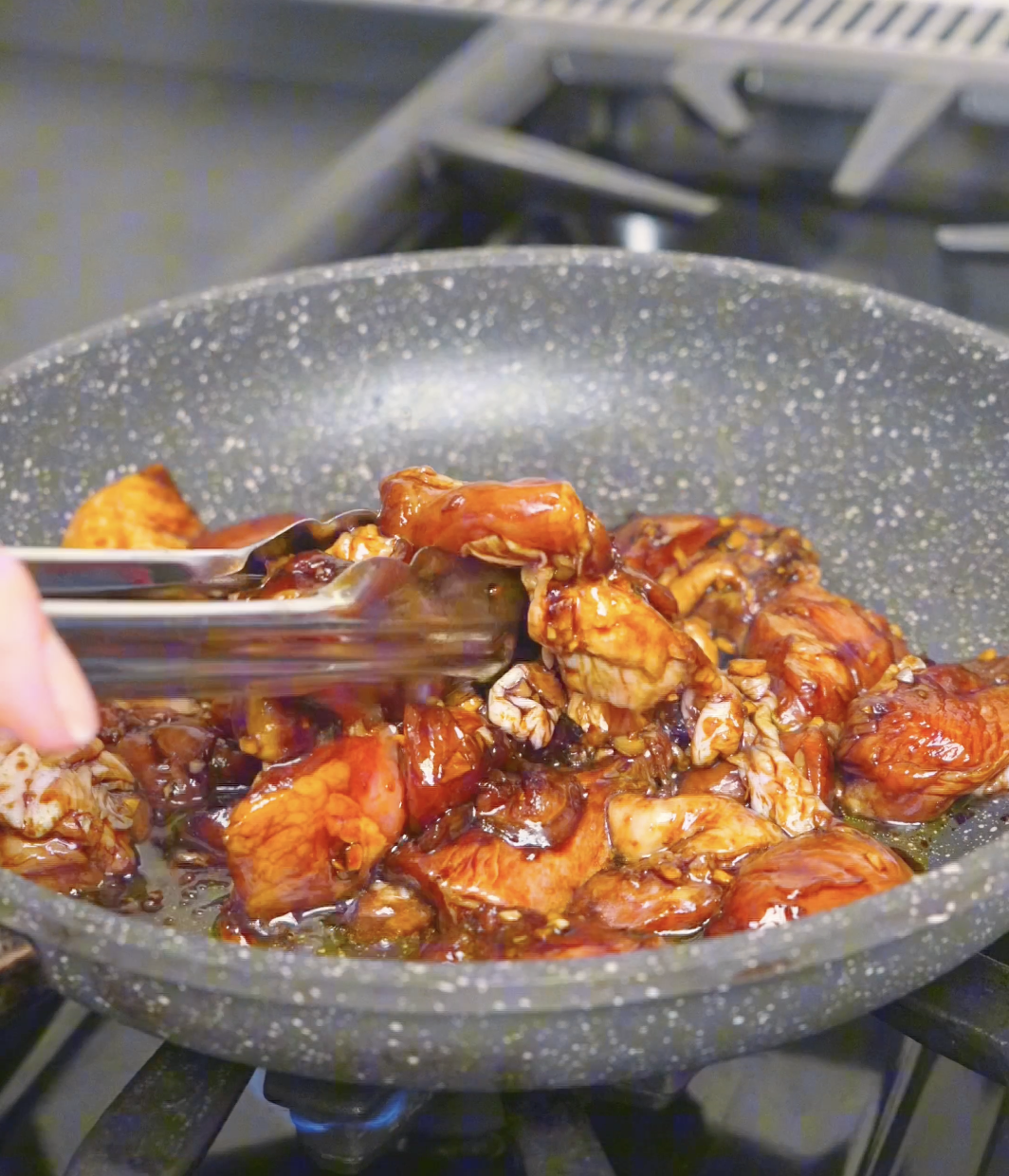 Marinated chicken thighs being turned with tongs in the pan while cooking Garlic Teriyaki Chicken Recipe.