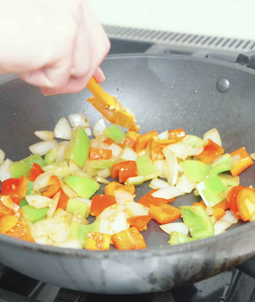 Onion chunks and red and green bell peppers being stirred in the pan for Black Pepper Steak Bites Recipe.