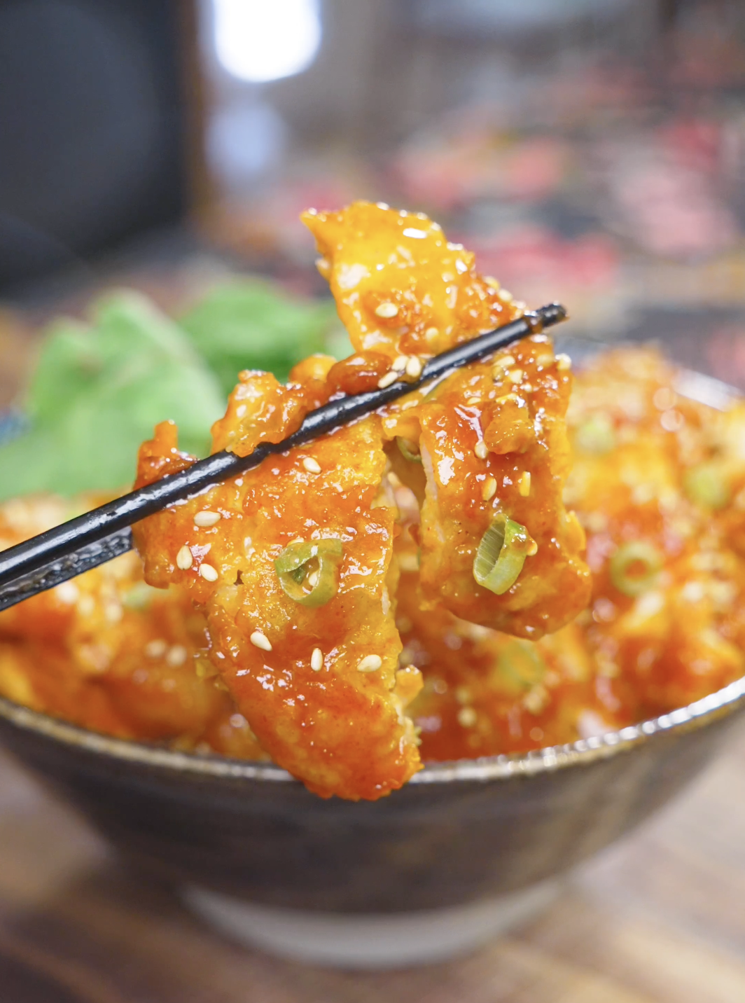 Chopsticks lifting a crisp, sauce-coated piece above the bowl of Creamy Gochujang Chicken Recipe.