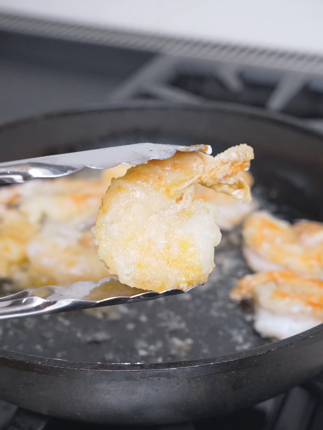 Tongs lifting a golden, crispy shrimp out of the oil for Salt and Pepper Shrimp Recipe.