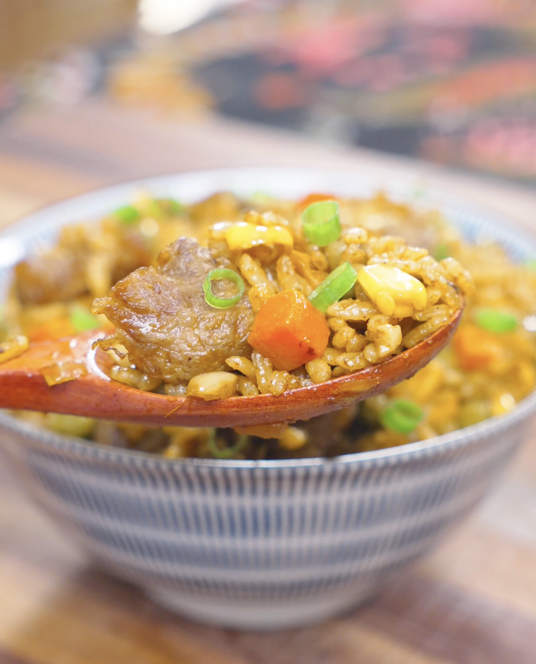 A wooden spoon lifting beef, carrots, and curry-coated rice from the bowl of Curry Fried Rice Recipe.