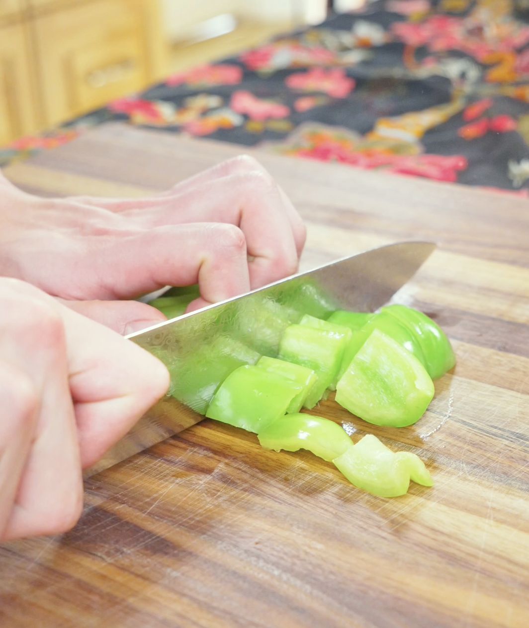 Green bell pepper being cut into thick chunks on a wooden board for Black Pepper Steak Bites Recipe.