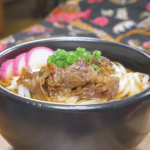 Finished Beef Udon Recipe in a black bowl with soy-glazed beef, fish cake, and scallions.