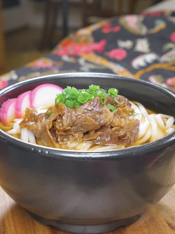 Finished Beef Udon Recipe in a black bowl with soy-glazed beef, fish cake, and scallions.