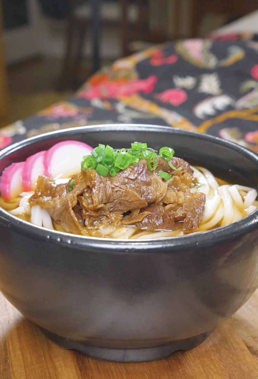Finished Beef Udon Recipe in a black bowl with soy-glazed beef, fish cake, and scallions.