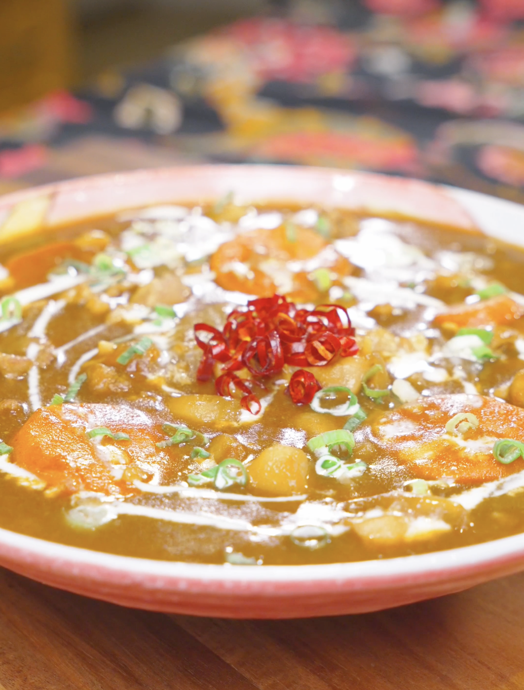 Finished Chicken Curry Stew Recipe in a pink bowl with cream, scallions, and dried peppers.