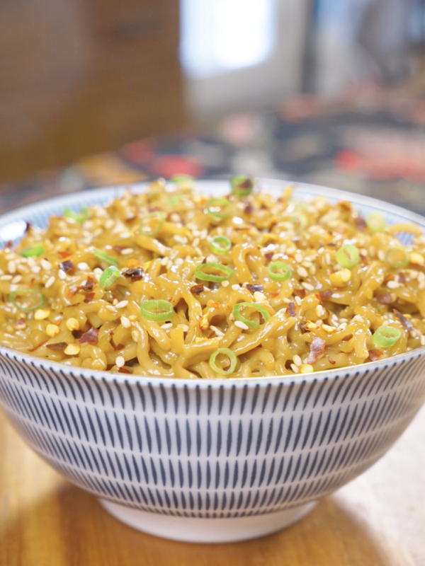 Finished Creamy Curry Noodles Recipe in a patterned bowl topped with sesame seeds, scallions, and red chili flakes.