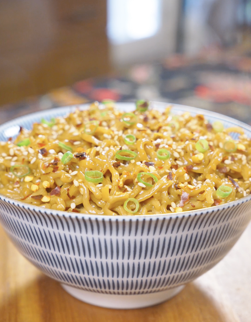 Finished Creamy Curry Noodles Recipe in a patterned bowl topped with sesame seeds, scallions, and red chili flakes.