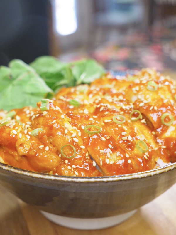 Finished Creamy Gochujang Chicken Recipe sliced over rice with sesame seeds, scallions, and greens.