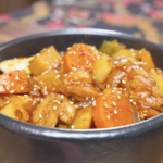 Finished Korean Braised Chicken Recipe in a black bowl with potatoes, carrots, and sesame seeds.
