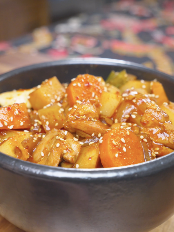 Finished Korean Braised Chicken Recipe in a black bowl with potatoes, carrots, and sesame seeds.
