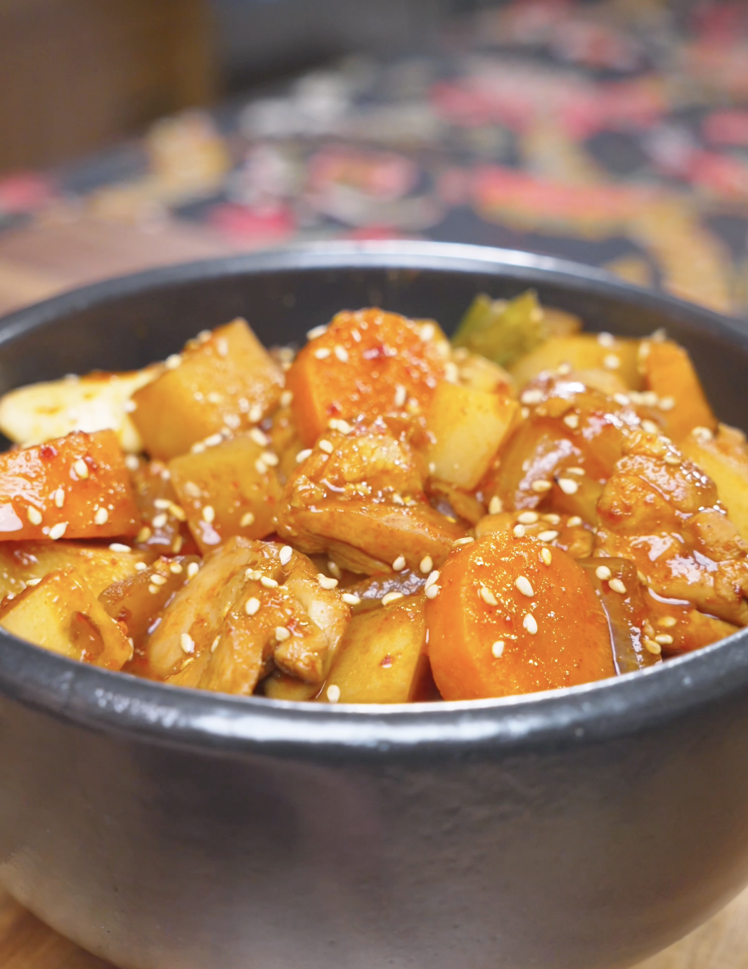 Finished Korean Braised Chicken Recipe in a black bowl with potatoes, carrots, and sesame seeds.
