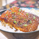Finished Spicy Salmon Bowl Recipe with chili crunch glazed salmon over rice, sesame seeds, scallions, and coleslaw mix.