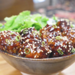 Finished Teriyaki Meatballs Recipe glazed and topped with sesame seeds and scallions, served with greens.