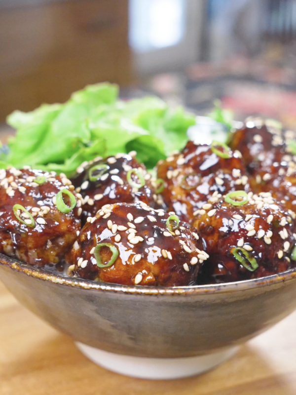 Finished Teriyaki Meatballs Recipe glazed and topped with sesame seeds and scallions, served with greens.