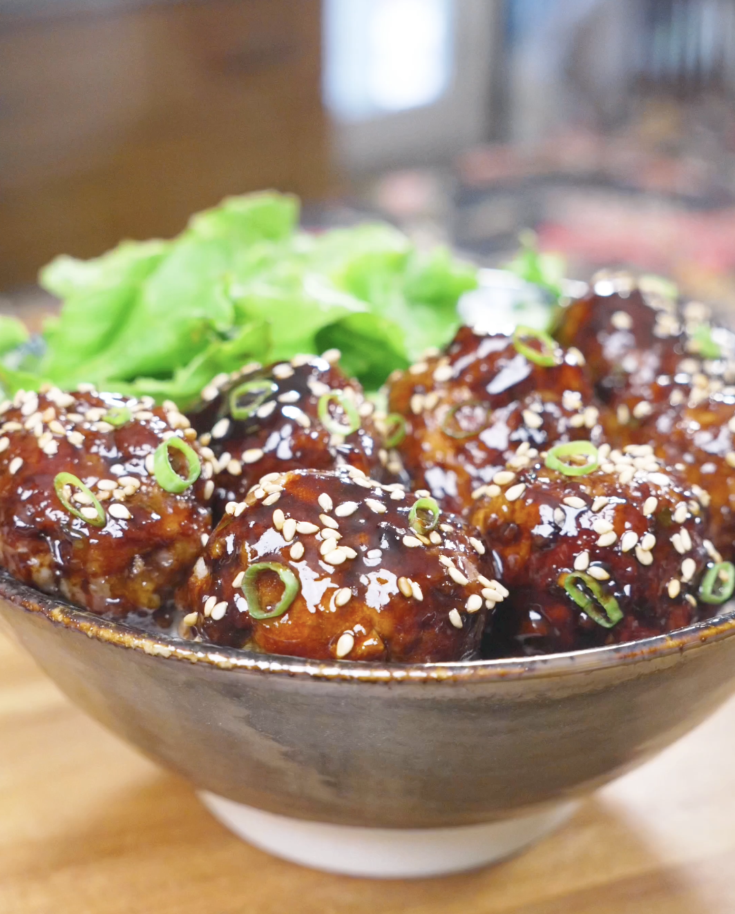 Finished Teriyaki Meatballs Recipe glazed and topped with sesame seeds and scallions, served with greens.