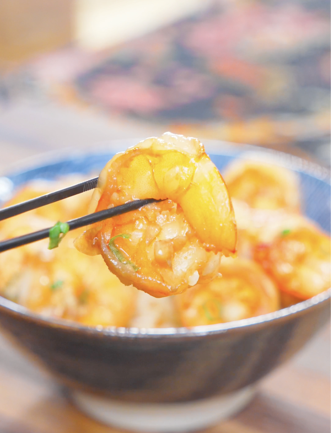 Chopsticks holding a single plump shrimp coated in minced garlic above the bowl of Garlic Butter Shrimp Recipe.