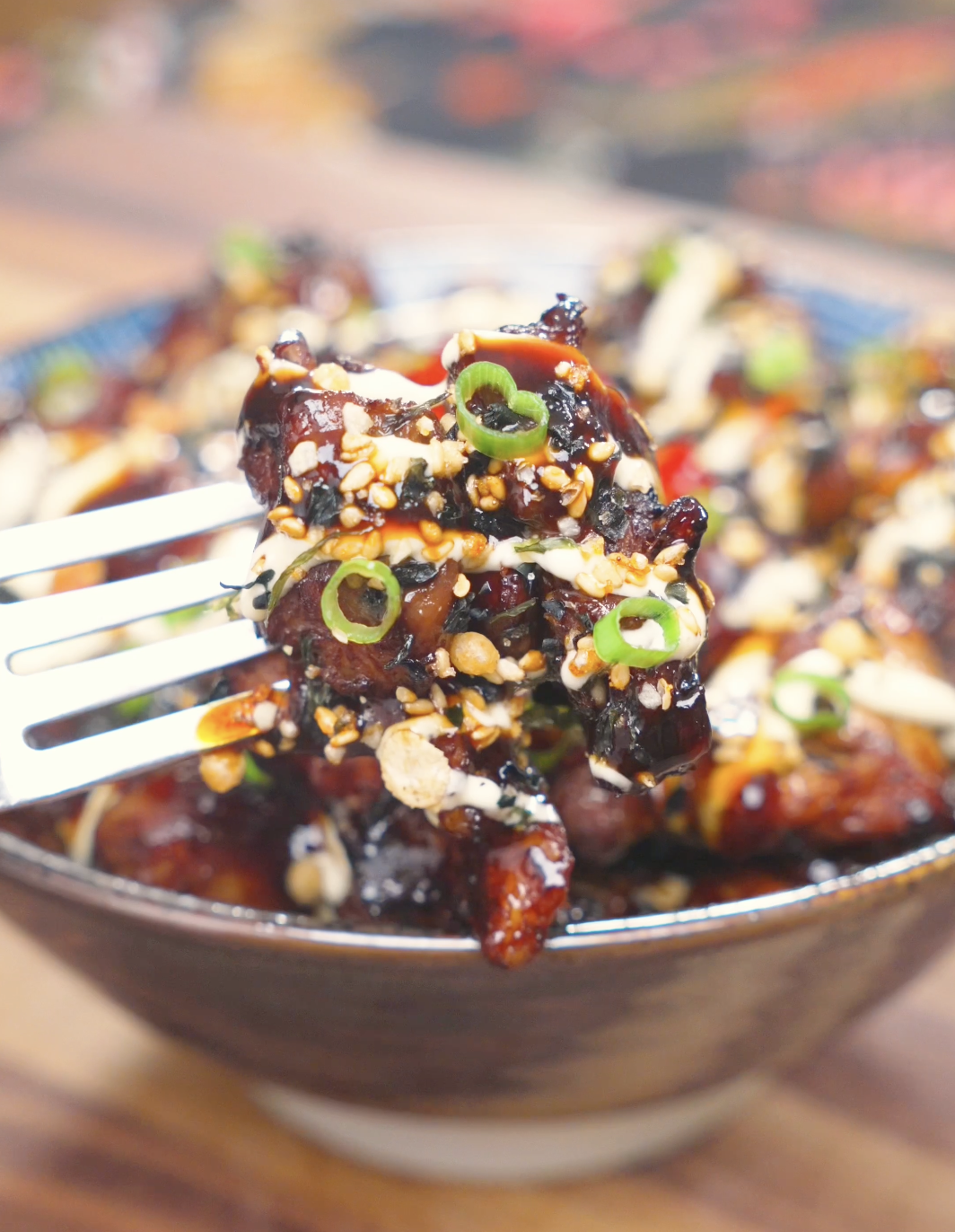 A fork lifting a glazed piece topped with mayo, furikake, and scallions above the bowl of Garlic Teriyaki Chicken Recipe.