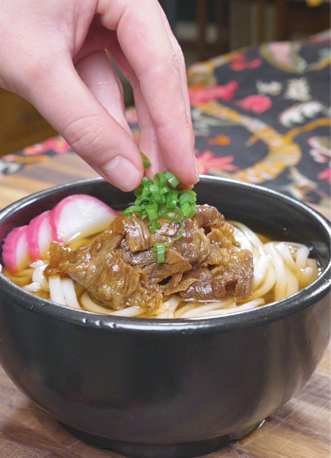 Sliced scallions being sprinkled over soy-glazed beef and noodles for Beef Udon Recipe.