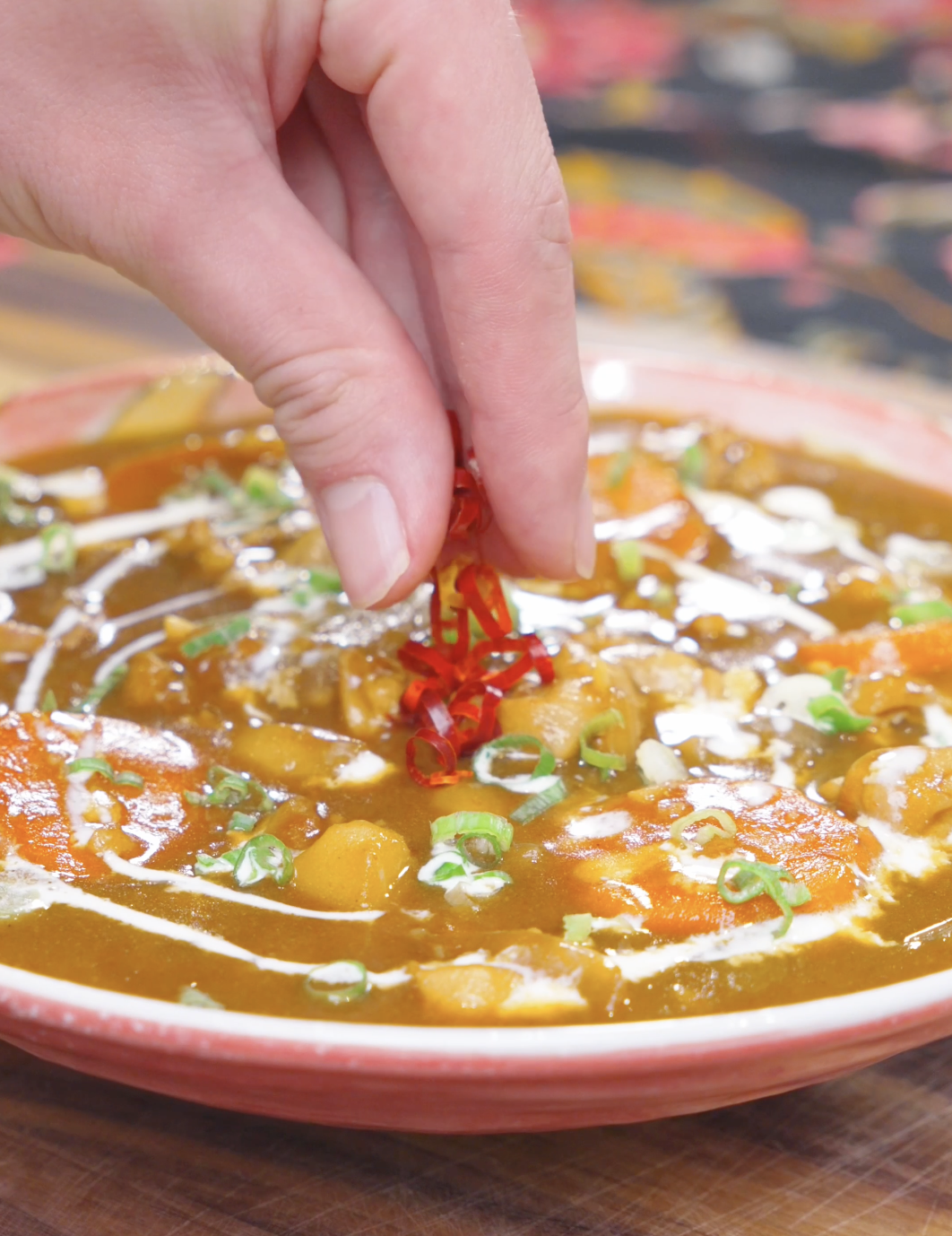Sliced red chilies being added over cream and scallions on a bowl of Chicken Curry Stew Recipe.