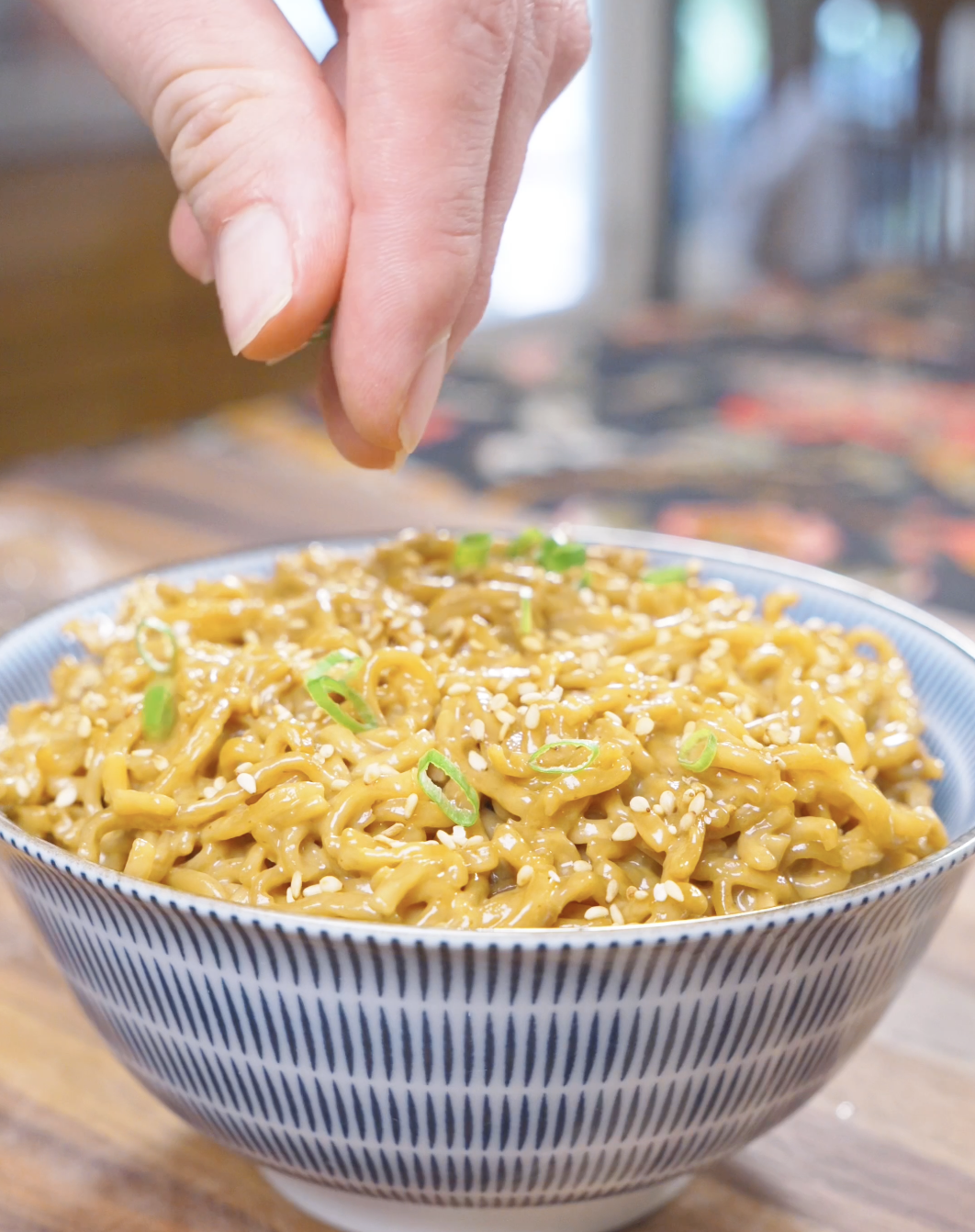 Sliced scallions being sprinkled over a sesame-topped bowl of Creamy Curry Noodles Recipe.