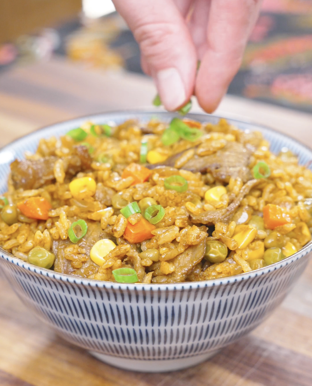 Sliced scallions being sprinkled over a finished bowl of Curry Fried Rice Recipe.