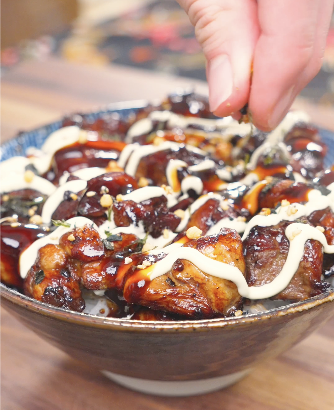 Furikake being sprinkled over kewpie mayo and soy glaze on a bowl of Garlic Teriyaki Chicken Recipe.