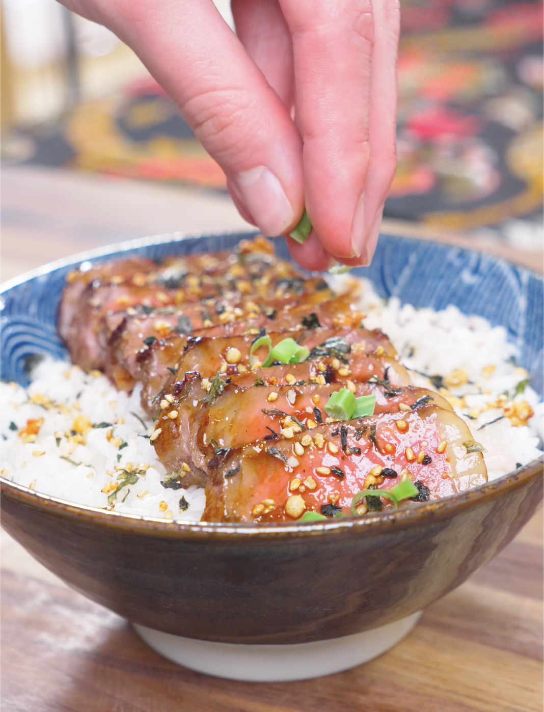 Sliced scallions being sprinkled over furikake-dusted rice and steak for Japanese Steak Bowl Recipe.