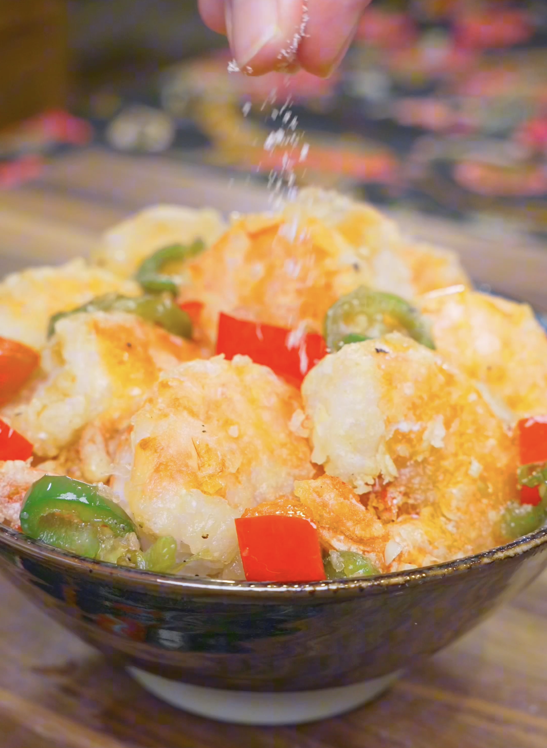 A final pinch of the seasoning mixture being sprinkled over the bowl of Salt and Pepper Shrimp Recipe.