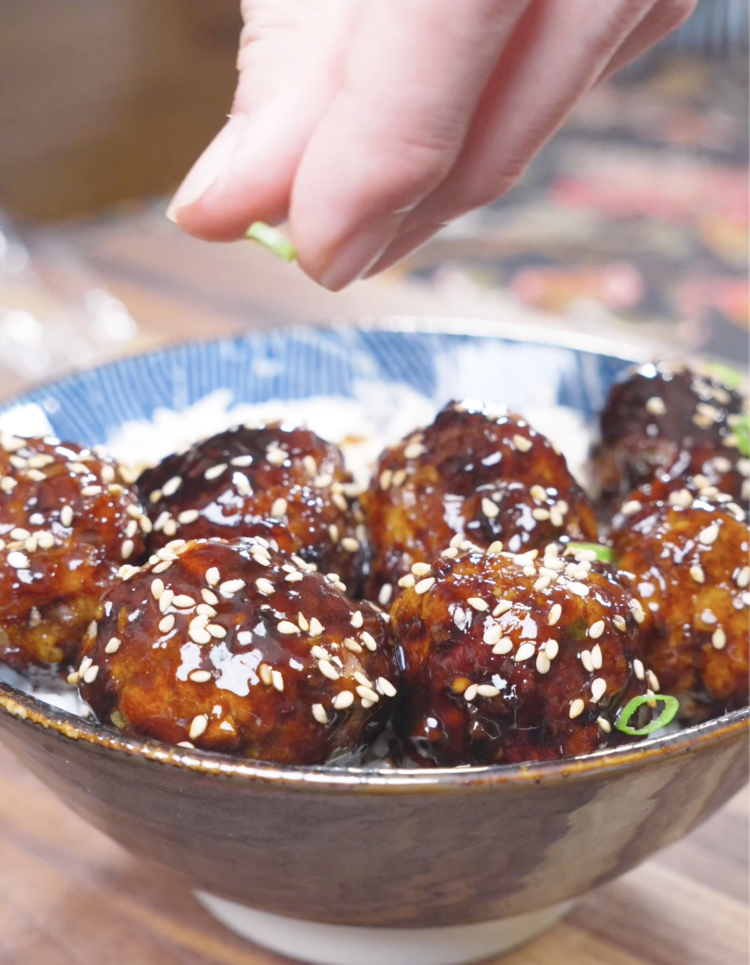 Sliced scallions being sprinkled over sesame-topped glazed meatballs for Teriyaki Meatballs Recipe.