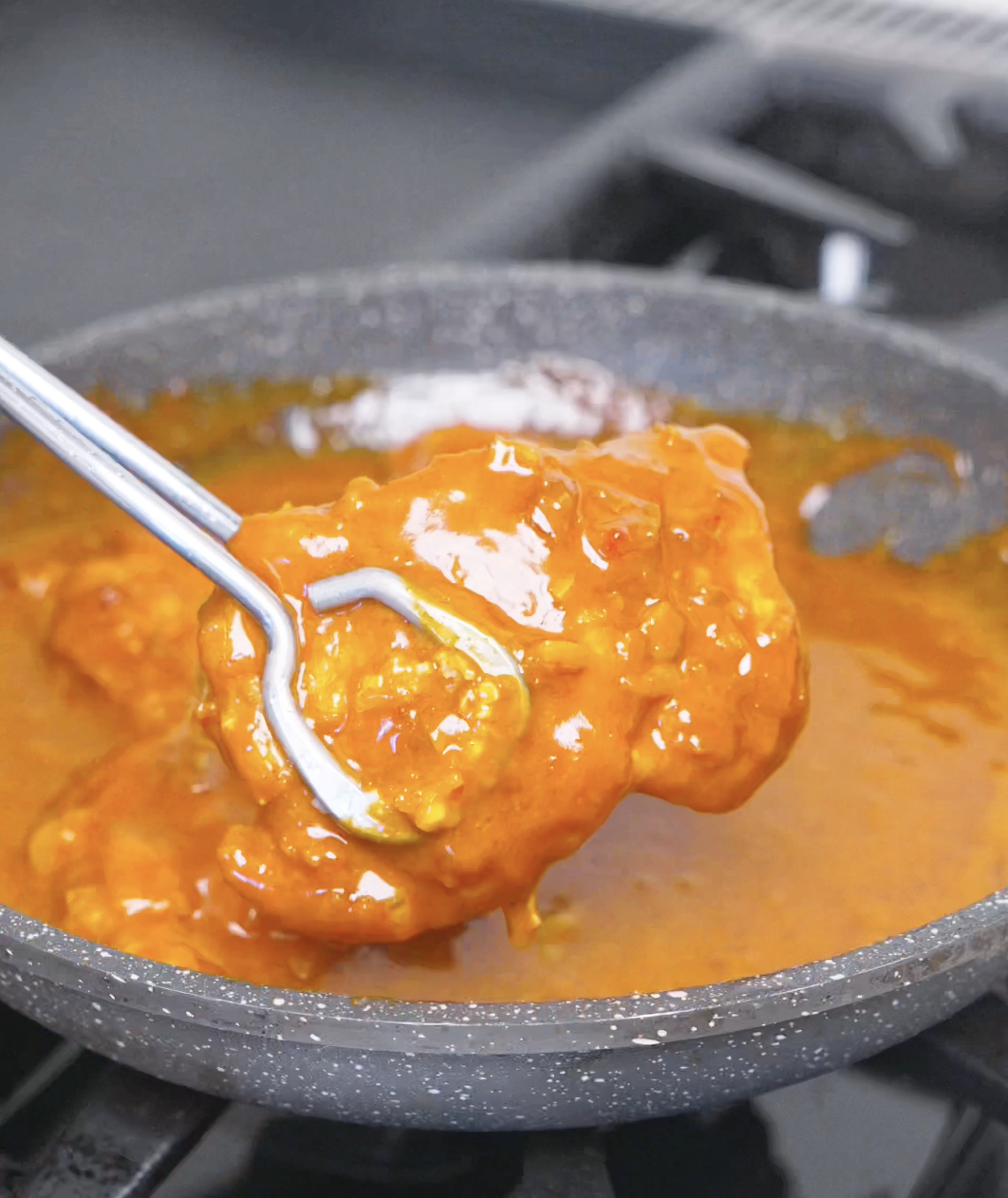 Fried chicken being turned in the pan until each piece is fully coated for Creamy Gochujang Chicken Recipe.