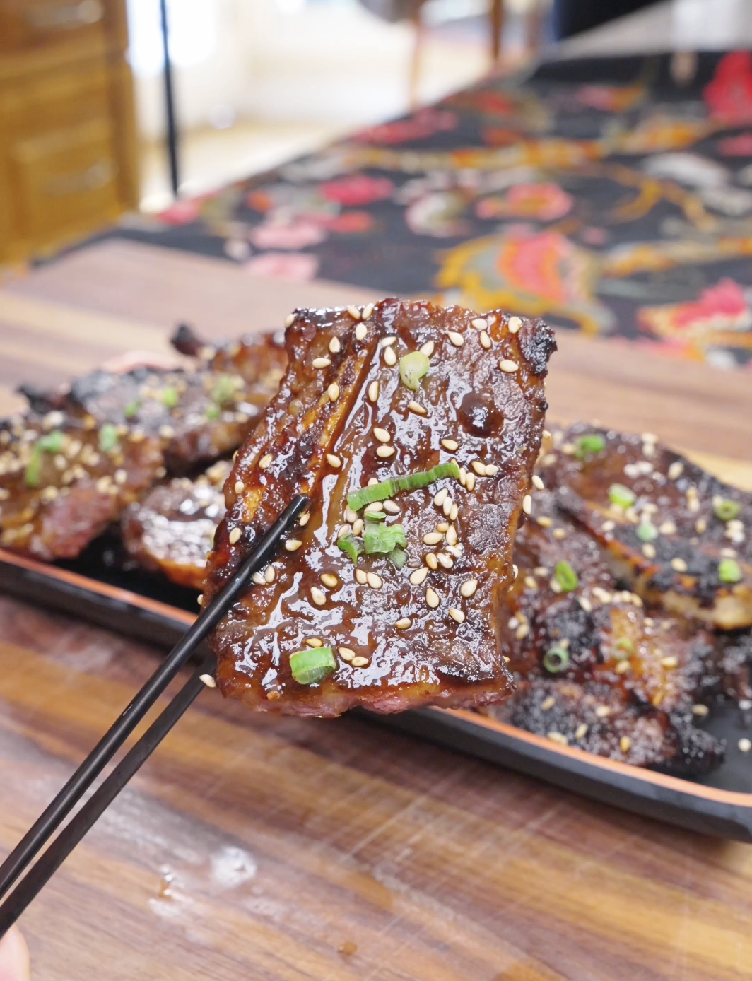 Chopsticks holding a glossy, sesame-topped piece above the platter of Korean BBQ Short Rib Recipe.