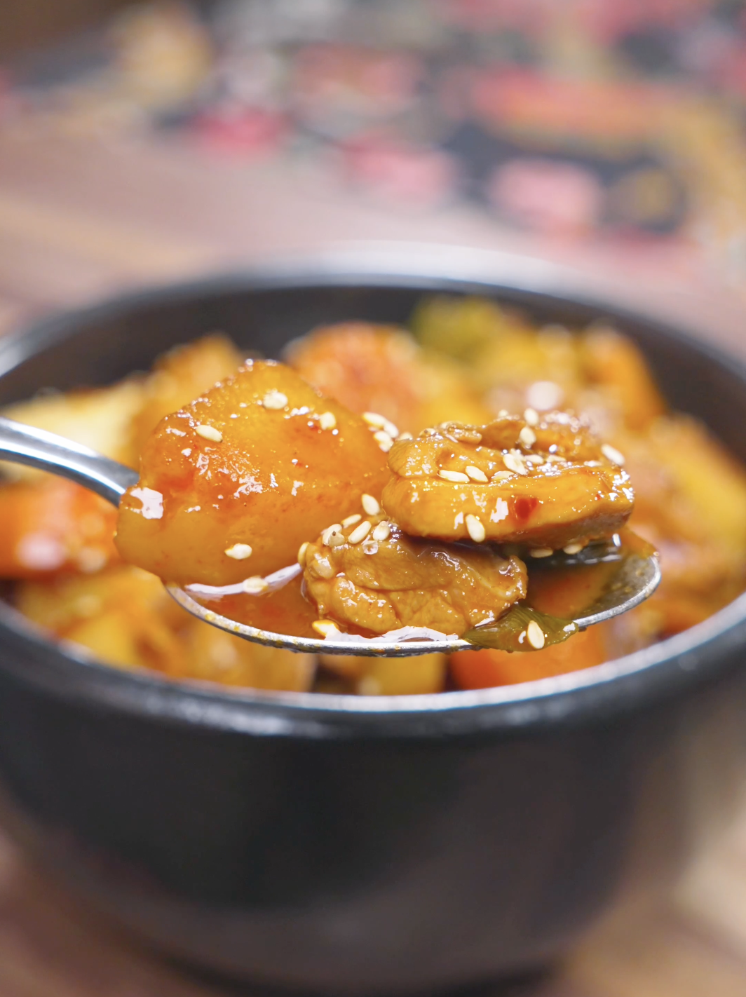 A spoon lifting a potato chunk and piece of chicken from the bowl of Korean Braised Chicken Recipe.