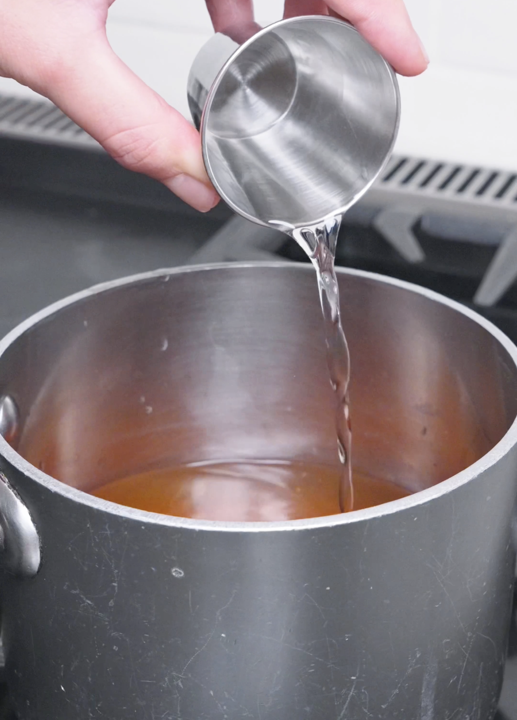 Mirin being poured into the dashi, soy sauce, and sugar broth in a pot for Beef Udon Recipe.