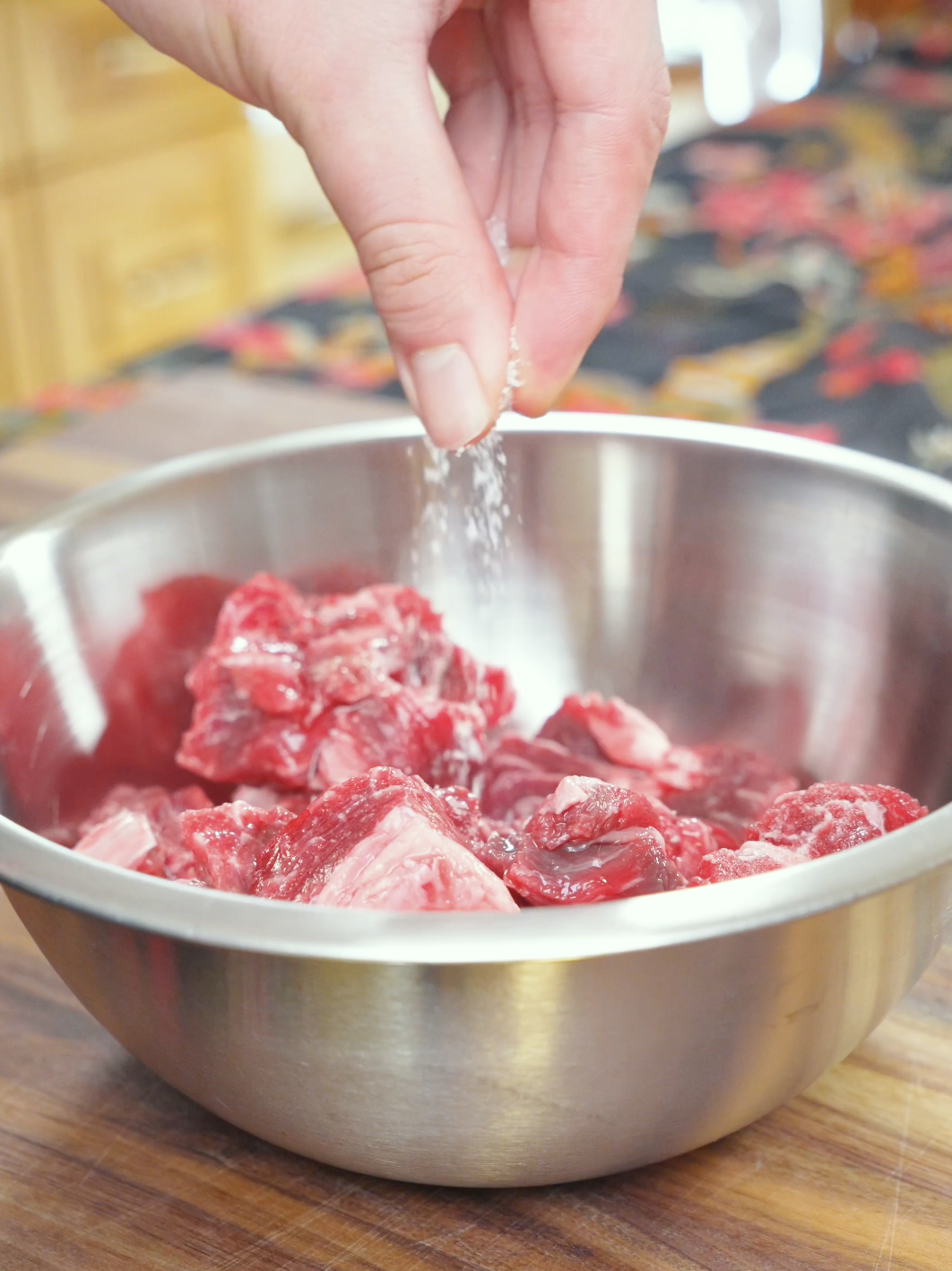 Salt being sprinkled over cubed raw steak in a metal bowl while marinating it for Black Pepper Steak Bites Recipe.