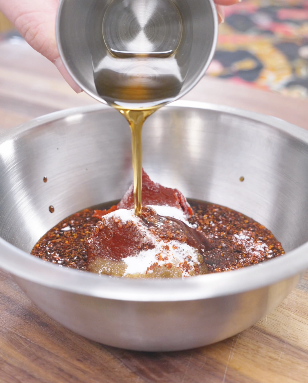 Sesame oil being poured over gochujang, gochugaru, and sugar in a bowl for Korean Braised Chicken Recipe.