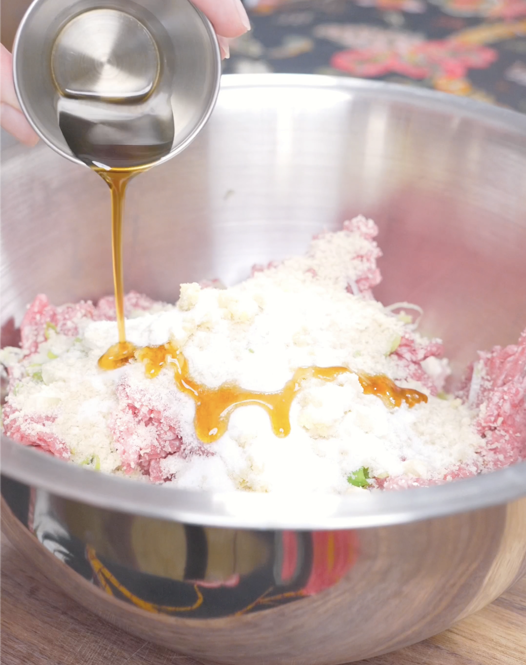 Sesame oil being poured over ground meat, panko, scallions, and seasoning for Teriyaki Meatballs Recipe.