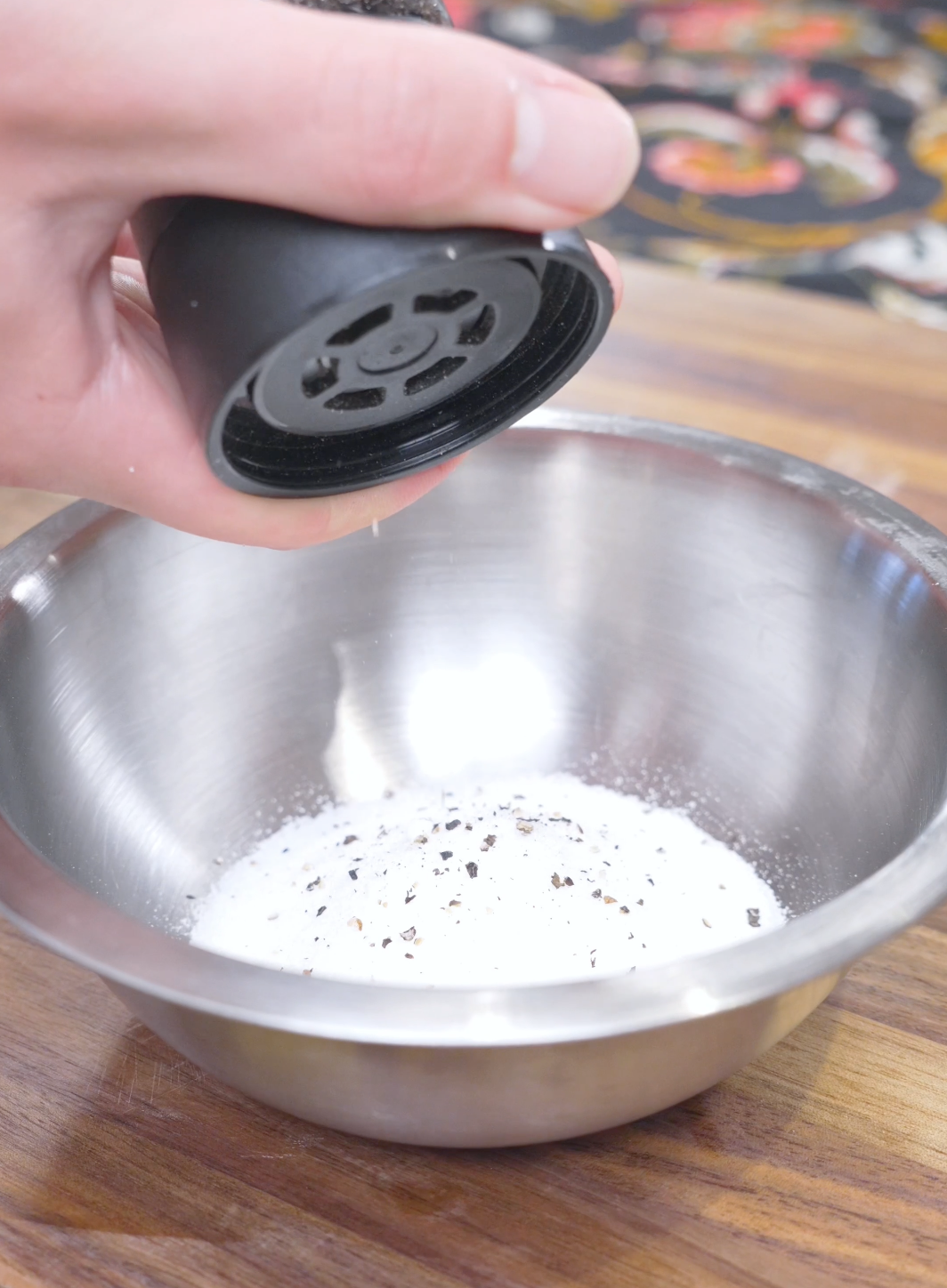 Black pepper being ground over salt and sugar in a metal bowl for Salt and Pepper Shrimp Recipe.