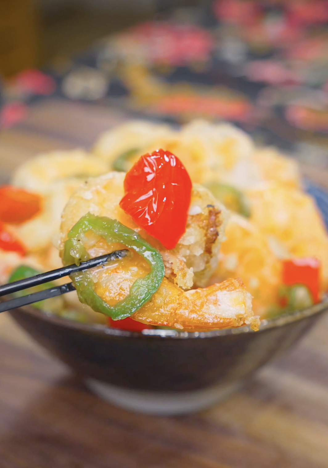 Chopsticks lifting a crispy shrimp with jalape&ntilde;o and red pepper above the bowl of Salt and Pepper Shrimp Recipe.